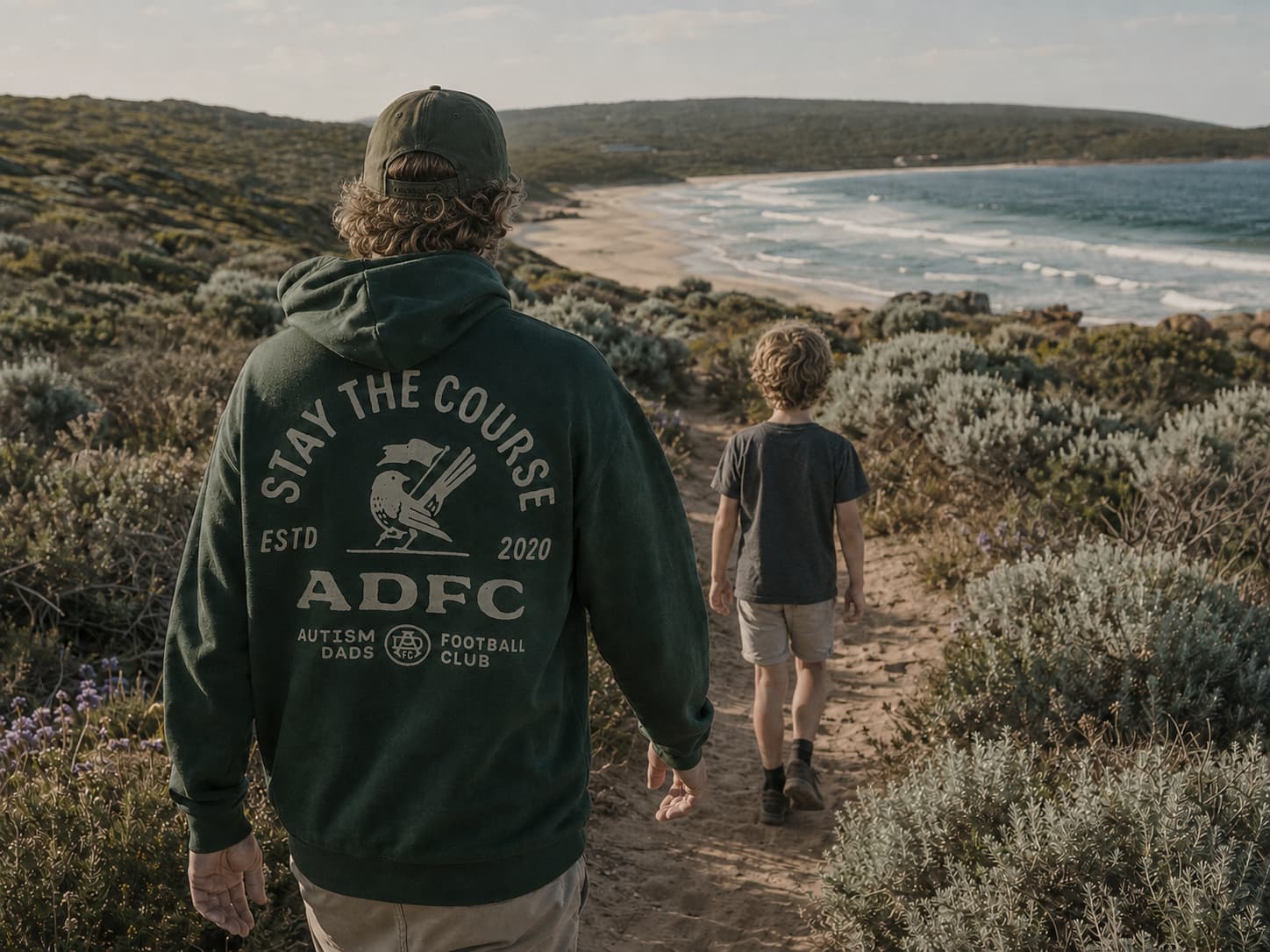 An ADFC dad and his son walking a coastal trail at dusk, wearing the ADFC jumper.